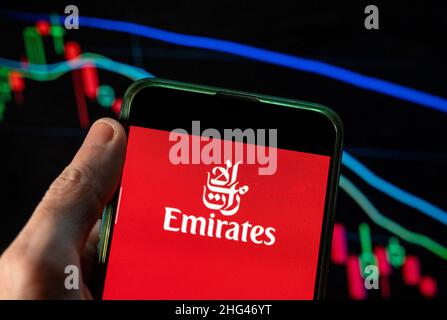 In questa illustrazione della foto, il logo della compagnia aerea degli Emirati Arabi Uniti è visualizzato su uno smartphone con un grafico dell'indice delle borse economiche sullo sfondo. Foto Stock