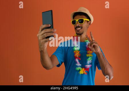 Uomo nero in costume per il carnevale brasiliano che tiene mobile isolato su sfondo arancione. Foto Stock