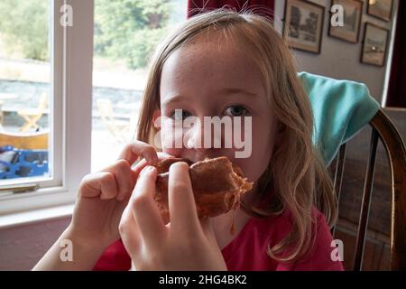 giovane ragazza di sette anni che mangia il budino dello yorkshire che gocciola con sugo di carne in un pub nel distretto del lago, cumbria, inghilterra, regno unito Foto Stock