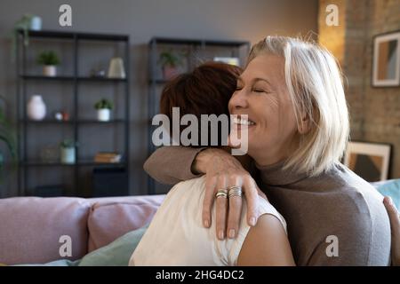 Donna anziana felice che abbraccia la sua amica mentre si trovano nella stanza, si salutano durante la riunione Foto Stock