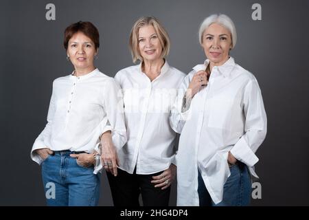 Ritratto di donne mature ed eleganti che si posano insieme alla fotocamera sullo sfondo grigio Foto Stock