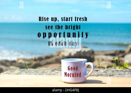 Citazione motivazionale e ispiratrice con una tazza di caffè sullo sfondo sfocato dell'oceano: Alzati, inizia a fresco e scopri le opportunità luminose di ogni giorno. Foto Stock