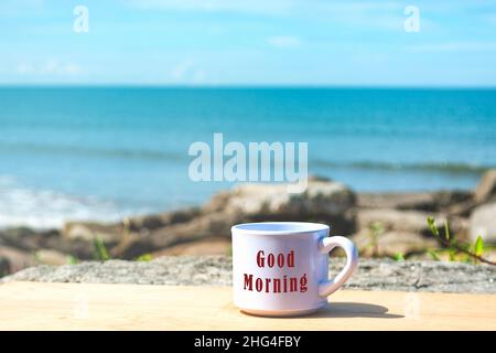 Buon testo del mattino su una tazza di caffè bianca con sfondo blu scuro dell'oceano Foto Stock