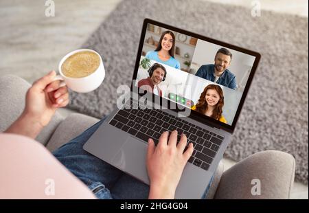 Donna irriconoscibile che ha una chat video con gli amici e bere un caffè Foto Stock