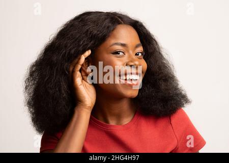 Curioso allegro Donna Nera con mano vicino orecchio cercando di ascoltare qualcosa Foto Stock