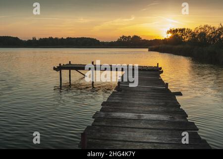 Tramonto su un lago tranquillo con un molo di legno Foto Stock