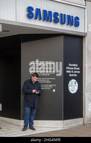 Uomo che utilizza il telefono cellulare all'ingresso del negozio Samsung chiuso su Princes Street, dopo essere stato trasferito nel nuovo quartiere St James, Edimburgo, Scozia, Regno Unito. Foto Stock