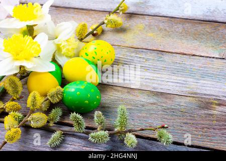 Composizione pasquale di fiori di narciso, rametti di salice fioriti e uova pasquali con un modello di fiori gialli e verdi su un retro legno backgroun Foto Stock