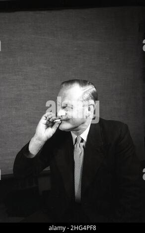 1950s, storico, un uomo in abito e cravatta, forse un attore, seduto da un palco con una sigaretta, Inghilterra, Regno Unito. Foto Stock