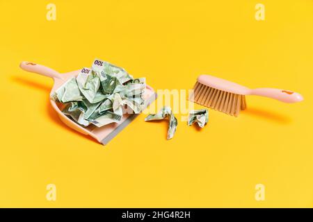 Layout creativo con pattumiera, scopa a mano e dollari di denaro sbriciolati su sfondo giallo. Finanza, corruzione, concetto di attività criminale Foto Stock