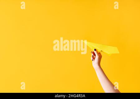 Una mano della donna tiene l'aeroplano di carta su sfondo giallo con spazio di copia Foto Stock