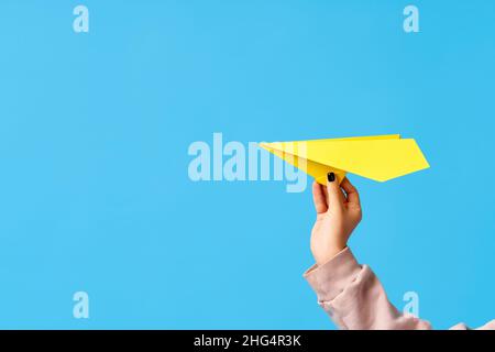 Una mano di donna tiene velivolo di carta giallo su sfondo blu con spazio di copia Foto Stock