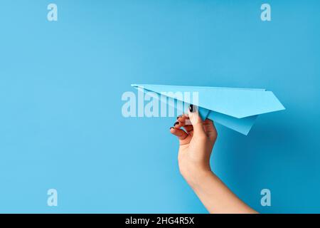 La mano di una donna tiene velivolo di carta blu su sfondo blu con spazio di copia Foto Stock