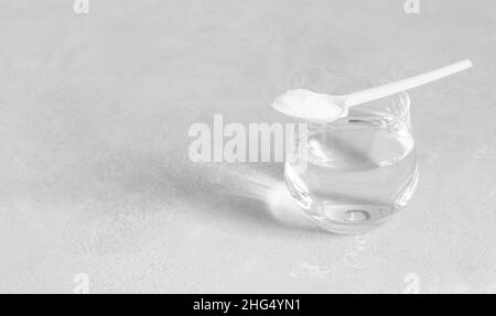 Collagene su sfondo grigio. Collagene proteina in polvere in un cucchiaio e un bicchiere di acqua closeup. Banner. Spazio di copia Foto Stock