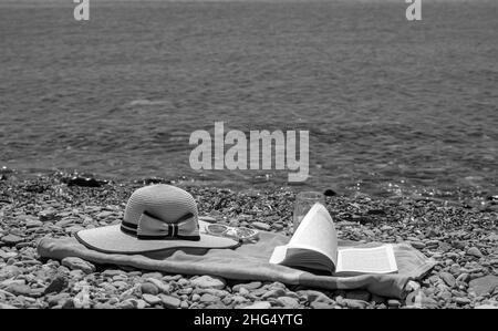 Concetto di vacanza estiva al mare con asciugamano, cappello e un libro, attività di svago in spiaggia in vacanza Foto Stock