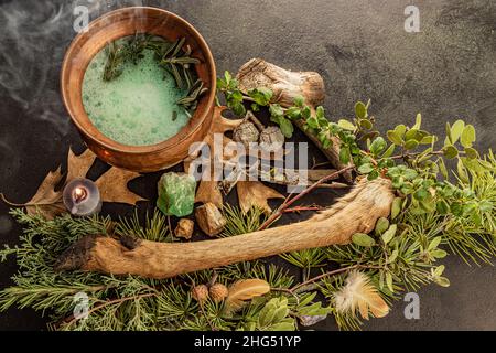 Calderone di rame pieno di pozione verde gorgogliante , una bacchetta magica con cristalli, candela che brucia, erba lora, oscura storia della strega, piatto occulto Foto Stock