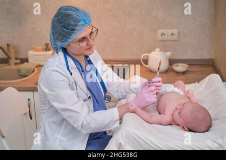 Il medico usa una siringa per iniettare un neonato. Un'infermiera in uniforme si prepara a vaccinare un bambino Foto Stock