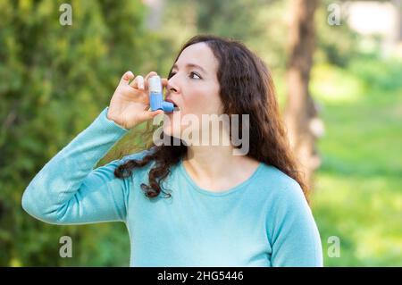 La donna sta usando un inalatore di asma in un parco Foto Stock