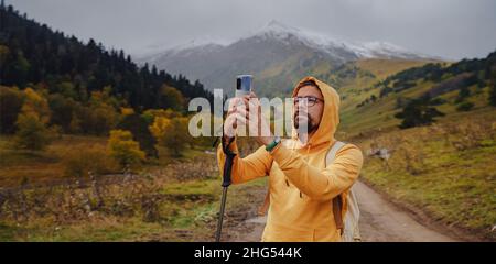 L'uomo crea splendide foto sullo smartphone per i social network. Stile di vita vagante, concetto di avventura vacanza autunnale all'aperto, da solo in natura. Viaggia verso il Caucaso settentrionale, Arkhyz, Russia Foto Stock