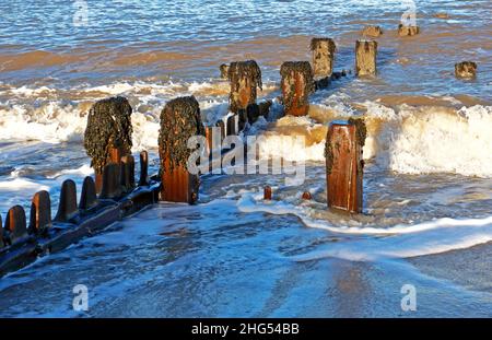 Onde che si infrangono intorno ad un vecchio frangiflutti con legname erodente sulla costa nord del Norfolk a Cart Gap, Happisburgh, Norfolk, Inghilterra, Regno Unito. Foto Stock