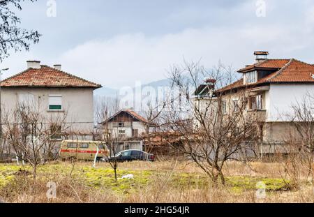 Piccolo villaggio con case tradizionali e veicoli vecchi in una zona povera nella campagna bulgara durante la stagione invernale. Bulgaria meridionale, Balcani, Europa. Foto Stock