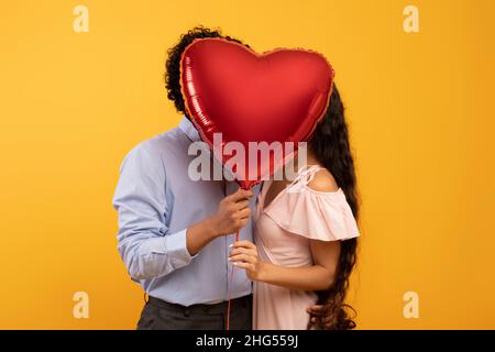 Romanticismo, amore, anniversario o giorno di San Valentino. Lovilng coppia indiana baciare e chiudere con palloncino di cuore Foto Stock