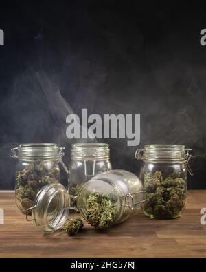 Colpo verticale di vasetti di vetro di stoccaggio, riempiti di germogli di cannabis, in una nuvola di fumo. Foto Stock