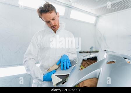 Auto Painter confronta il colore del paraurti di un'auto con le sfumature dei campioni Foto Stock