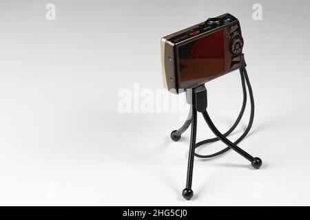 fotocamera compatta digitale con cinghia e display posteriore vuoto su cavalletto piccolo isolano su sfondo bianco. Foto Stock