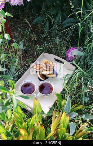 Tè in stile country nel giardino estivo nel villaggio. Due tazze di tè nero caldo e cupcake su vassoio di legno alla luce del sole Foto Stock