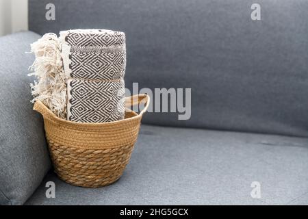 Tweed Plaid arrotolato in un cestino di vimini su un divano grigio Foto Stock