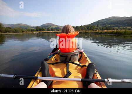giovane ragazza di sette anni che indossa giubbotto salvagente davanti a un kayak per due persone a windermere nel distretto estivo dei laghi, cumbria, inghilterra, regno unito Foto Stock