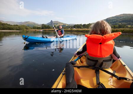 giovane ragazza di sette anni che indossa giubbotto di salvataggio davanti a un kayak da due persone come pagaia uomo passato a windermere nel distretto estivo del lago, cumbria, en Foto Stock