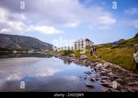 Circa 2020: Una capanna sul lago di Rila sentiero escursionistico in Bulgaria. La gente cammina vicino al lago. Splendido paesaggio naturale mozzafiato. Foto di alta qualità Foto Stock