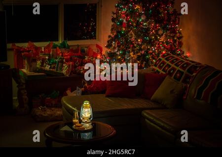 Una scena di Natale in soggiorno notturna con un albero decorato, regali, latte e biscotti per Babbo Natale. Foto Stock