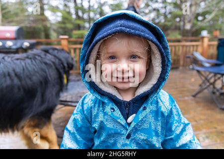 Testa e spalle vista di un ragazzo felice sorridente. Giacca blu di tre anni con due cappe per mantenere caldo all'aperto durante l'inverno. Foto Stock