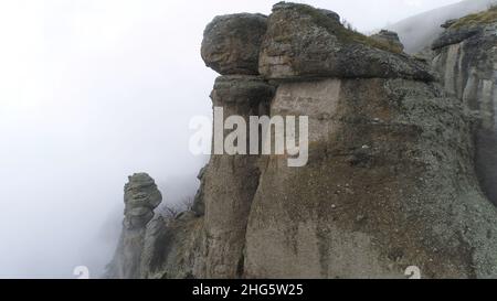 Montagne maestose nelle nuvole con alberi gialli e autunnali. Paesaggio con belle alte rocce e drammatica nebbia con alberi gialli, sfondo naturale. Foto Stock