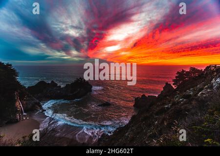 Fiery tramonto sulle acque blu di Big sur, CA a Mcway Falls Foto Stock