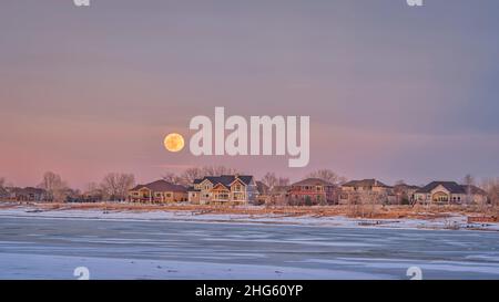 Luna piena che sorge sopra le case sul lungomare di Boyd Lake nel nord del Colorado, paesaggio invernale Foto Stock