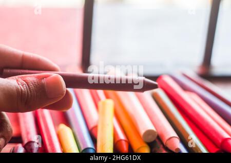 La diversità di colore del pastello focalizzata e la mano che raccoglie un pastello marrone, spazio di copia Foto Stock