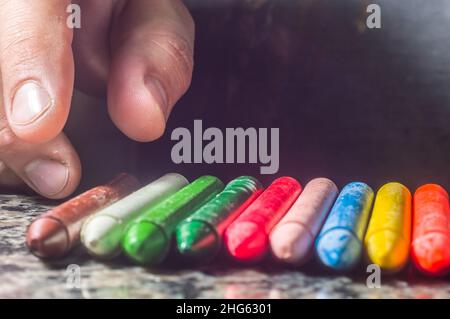 La diversità di colore del pastello focalizzata e la mano che raccoglie un pastello marrone, spazio di copia Foto Stock