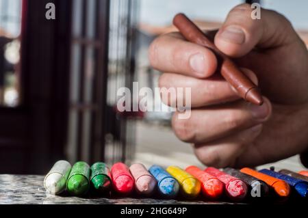 La diversità di colore del pastello focalizzata e la mano che raccoglie un pastello marrone, spazio di copia Foto Stock