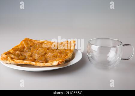 Bere tè. Un pezzo di torta di pera in un piattino e una tazza trasparente a doppia parete. Il concetto di minimalismo. Foto Stock