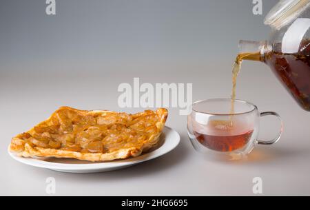 Bere tè. Un pezzo di torta di pera in un piattino e una tazza trasparente a doppia parete. Il tè nero appena fatto viene versato da una teiera in una tazza. Il co Foto Stock