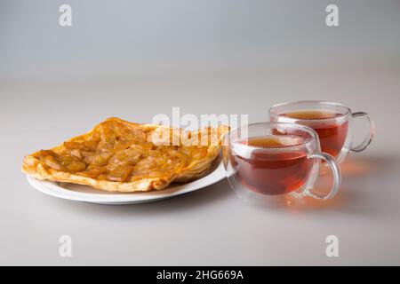 Bere tè. Un pezzo di torta di pera in un piattino e due tazze trasparenti a doppia parete con tè nero appena fatto. Il concetto di minimalismo. Foto Stock