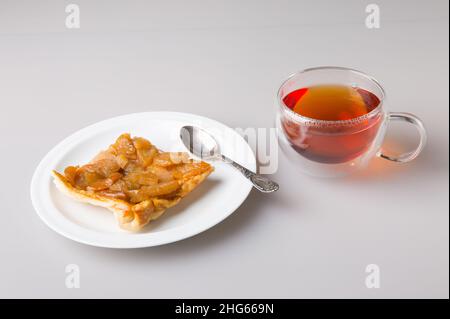 Bere tè. Un pezzo di torta di pera in un piattino e una tazza trasparente a doppia parete con tè nero appena fatto. Il concetto di minimalismo. Foto Stock