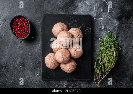 Polpette di vegano crude di carne vegetale con timo. Sfondo nero. Vista dall'alto Foto Stock
