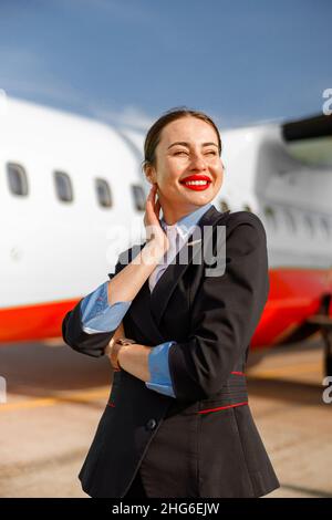 Gioioso assistente di volo donna in piedi all'aperto in campo aereo Foto Stock