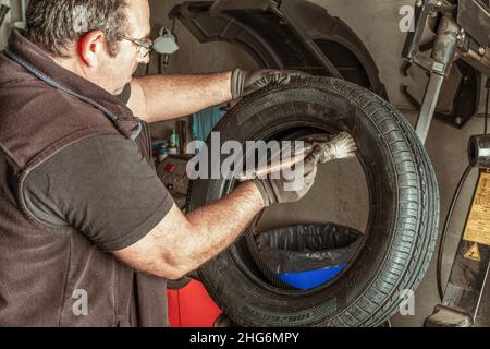 Uomo che applica lubrificante a uno pneumatico utilizzando una spazzola in un garage Foto Stock