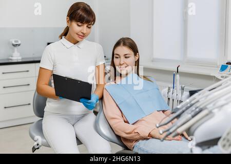 Dentista amichevole con compressa che spiega il trattamento al paziente durante l'esame dei denti. Moderna clinica dentale. Concetto di cura orale professionale, consultazione medica in studio di stomatologia. Foto Stock